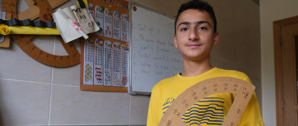 Syrian refugee and school pupil Omar stands in front of class whiteboard.
